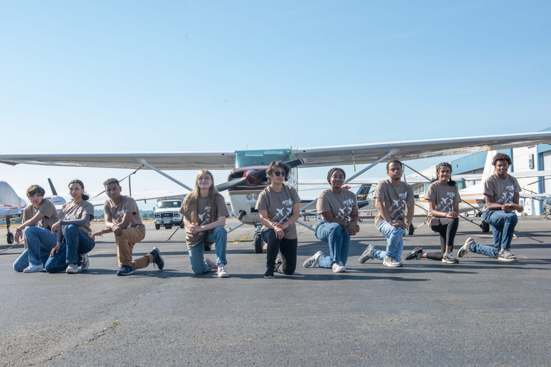 Red-Tailed Hawks Flying Club youth members kneeling in front of a training aircraft, representing diversity and unity in aviation education.