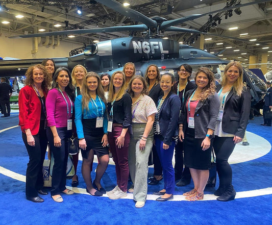 Group of Whirly-Girls International members standing in front of a helicopter at VERTICON, showcasing women in rotorcraft aviation.