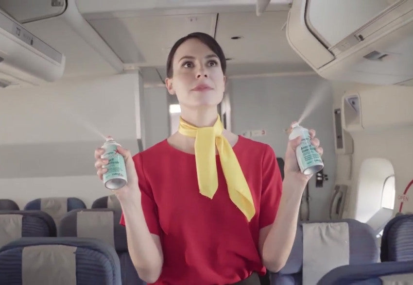 Flight attendant performing aircraft disinsection by spraying insecticide aerosols in an airplane cabin, following international health protocols.