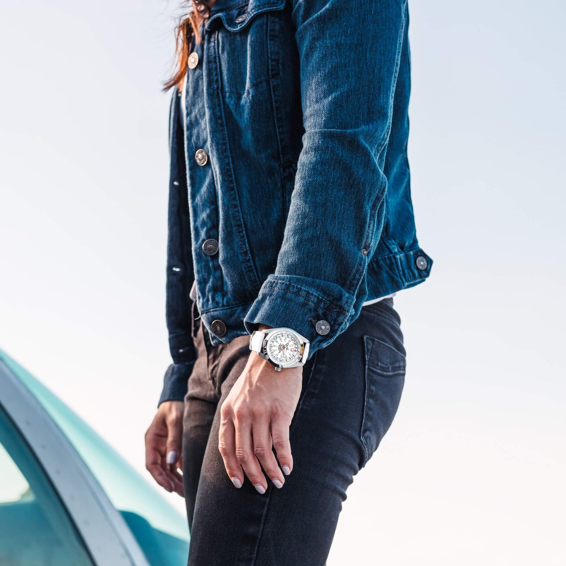 Amelia Women's Pilot Watch with Cloud White Dial and White Leather Strap, Shown on Wrist of Woman in Denim Jacket Standing Near Aircraft Canopy