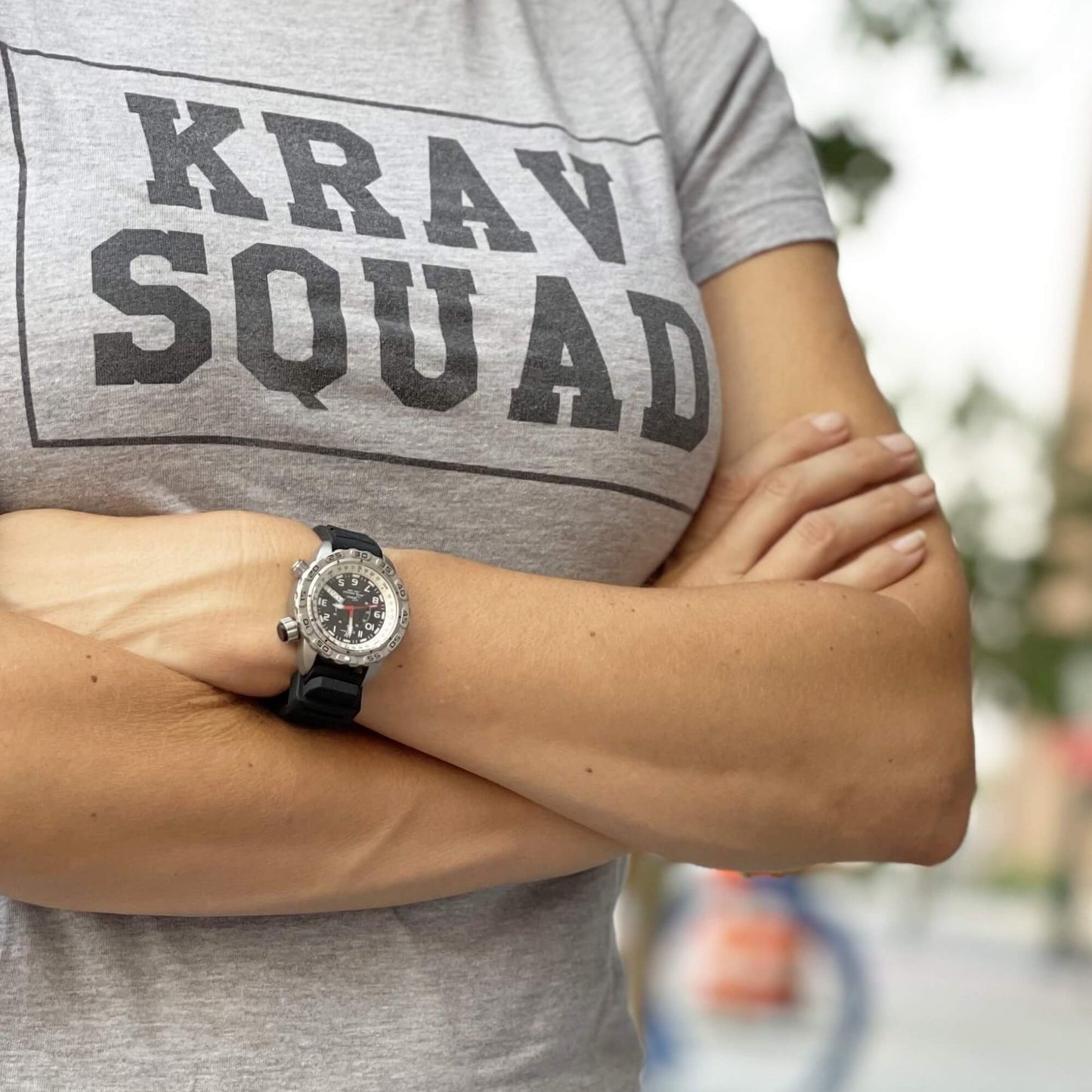 Jane “Covert” Tactical Watch on Wrist – Stainless Steel Case, Black Dial with Red Hands, and Black Silicone Strap Worn by Woman in Krav Maga Shirt