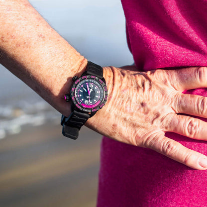 Nadia Abyss Automatic Dive Watch with Black Silicone Strap and Pink Compass Bezel, Shown on Wrist Outdoors near Water