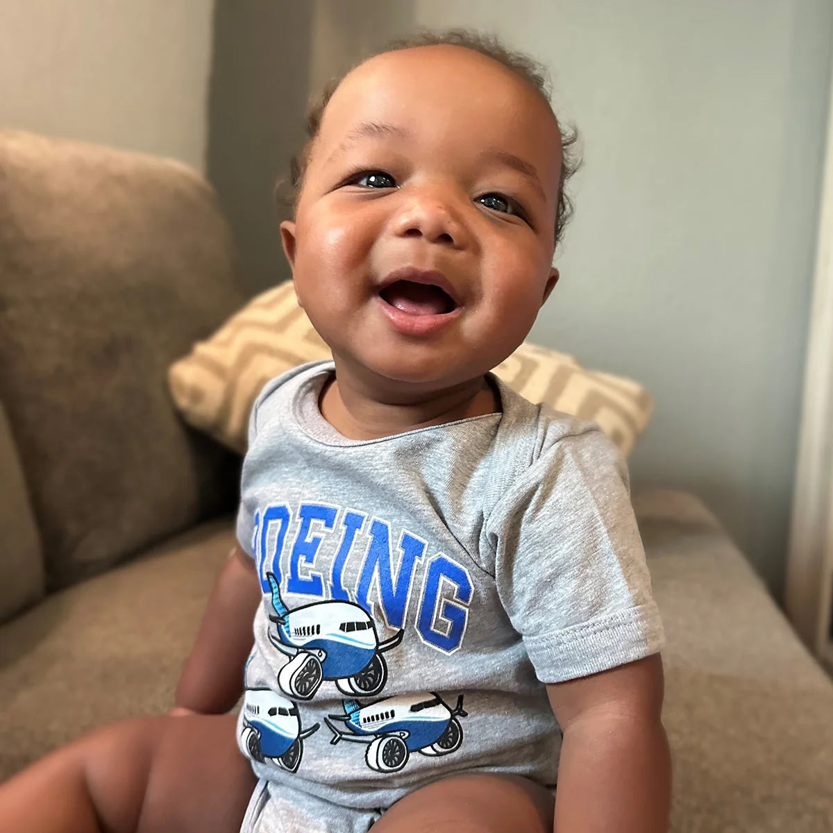 Baby wearing athletic grey Boeing Baby Varsity Pudgy Onesie with varsity logo and airplane design