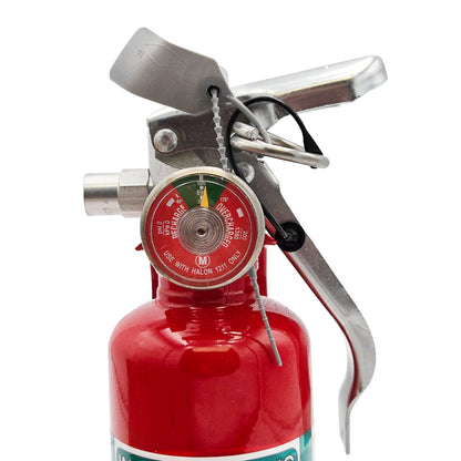 Close-up of H3R A344T Halon 1211 fire extinguisher top showing pressure gauge, silver handle, safety pin, tamper seal, and metal tag