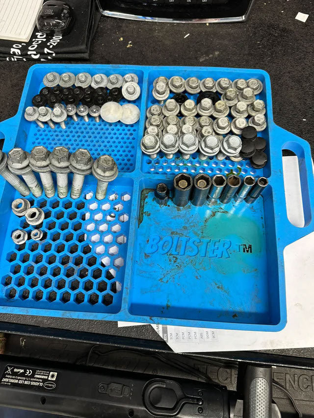 Blue Boltster™ Flexible Organizing Tray filled with large bolts and fasteners on a workbench during mechanical disassembly