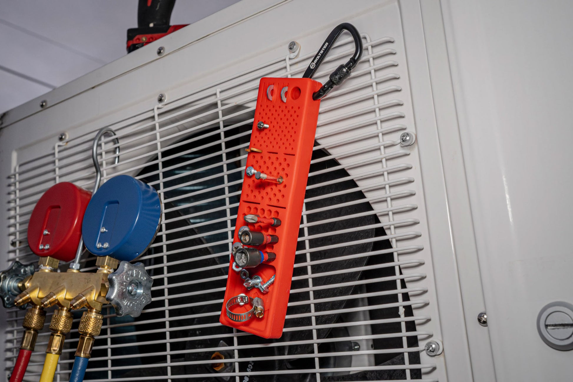Red Bitster 2.0 fastener organizer hanging on HVAC unit with screws, bits, and clips
