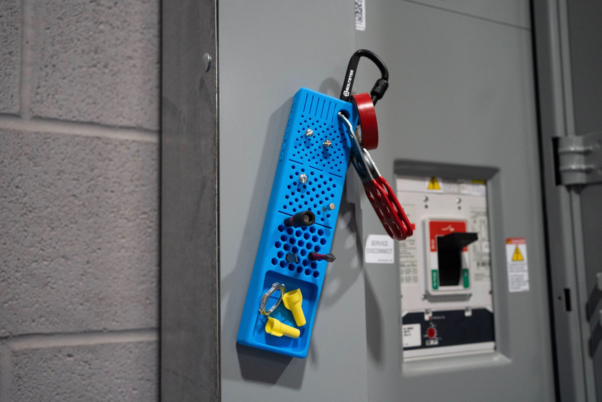 Blue Bitster 2.0 organizer magnetically mounted to electrical panel with wire connectors and small tools