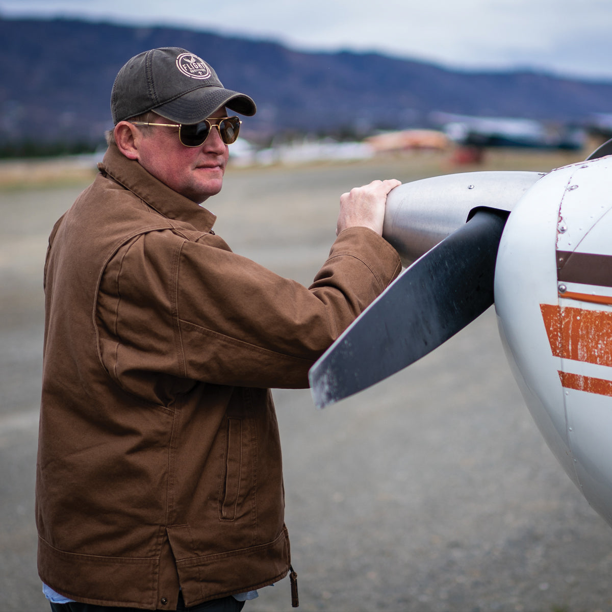 Side view of man wearing Flight Outfitters Bush Pilot Jacket with hand on aircraft propeller