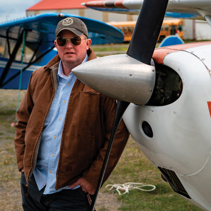 Man wearing Brown Flight Outfitters Bush Pilot Jacket leaning against aircraft