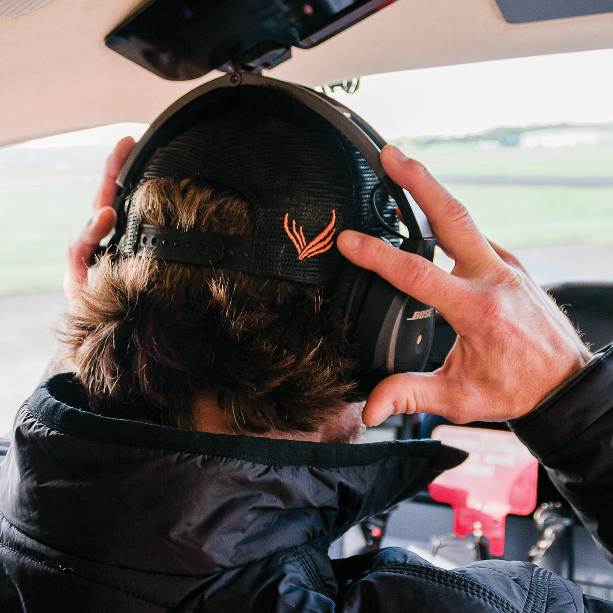 A man wearing the Flight Outfitters Chart Topo Hat with an aviation headset, emphasizing the back for comfort.
