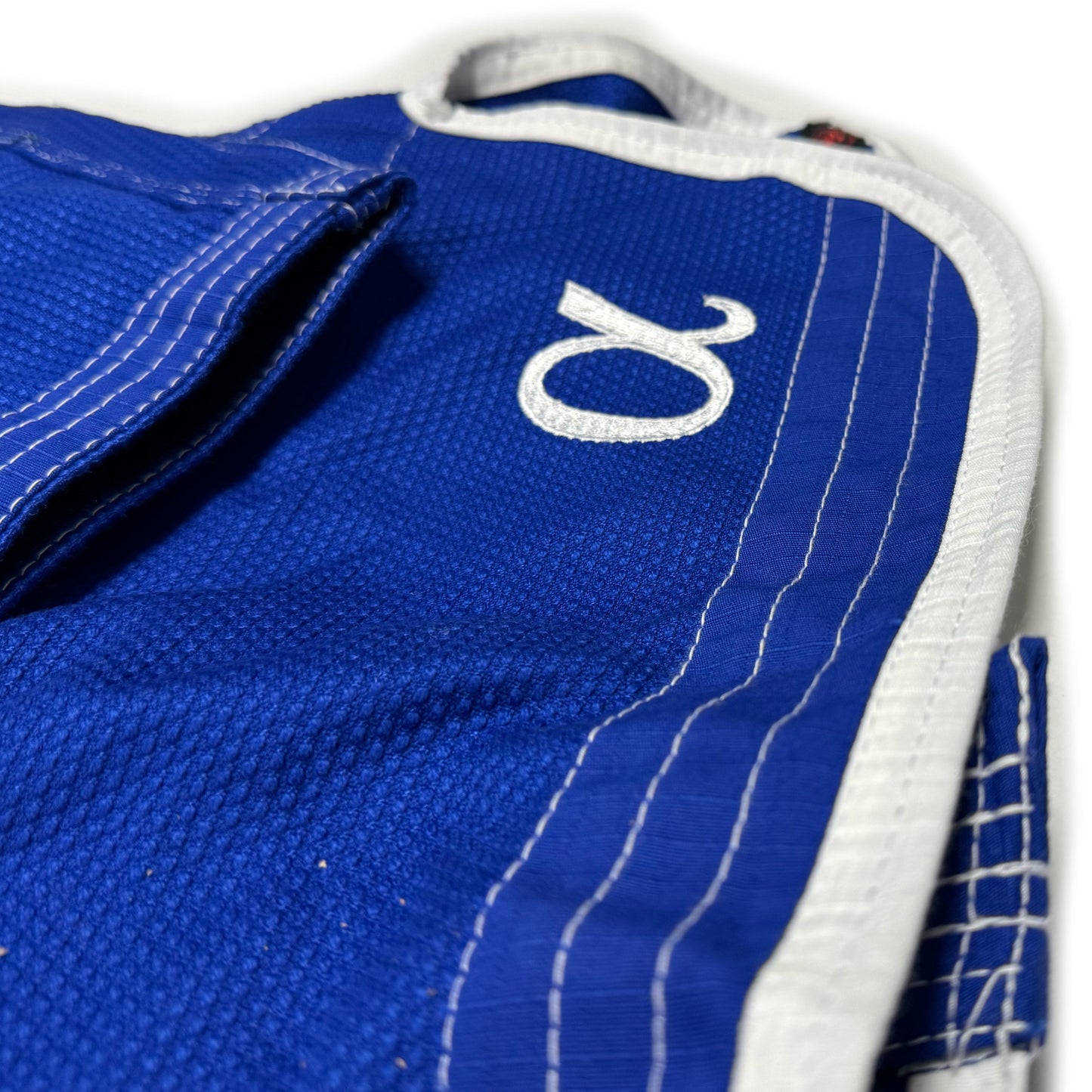Zed Honra Women’s Alpha Gi – Close-Up of Greek Letter Alpha and Reinforced Skirt Construction on Blue BJJ Kimono