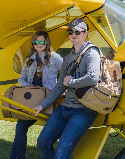 A man and woman standing under an aircraft wing, both carrying Flight Outfitters Bush Pilot Duffel Bags.