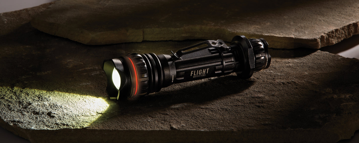 Flight Outfitters Bush Pilot Flashlight placed on rugged stones, emphasizing its durable, outdoor-ready construction.