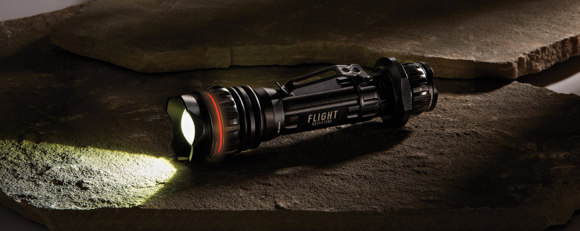 Flight Outfitters Bush Pilot Flashlight placed on rugged stones, emphasizing its durable, outdoor-ready construction.