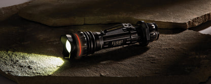 Flight Outfitters Bush Pilot Flashlight placed on rugged stones, emphasizing its durable, outdoor-ready construction.