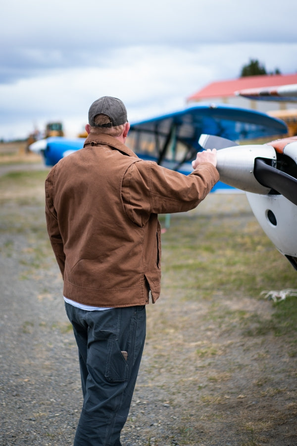 Back view of man wearing Flight Outfitters Bush Pilot Jacket with hand on aircraft propeller