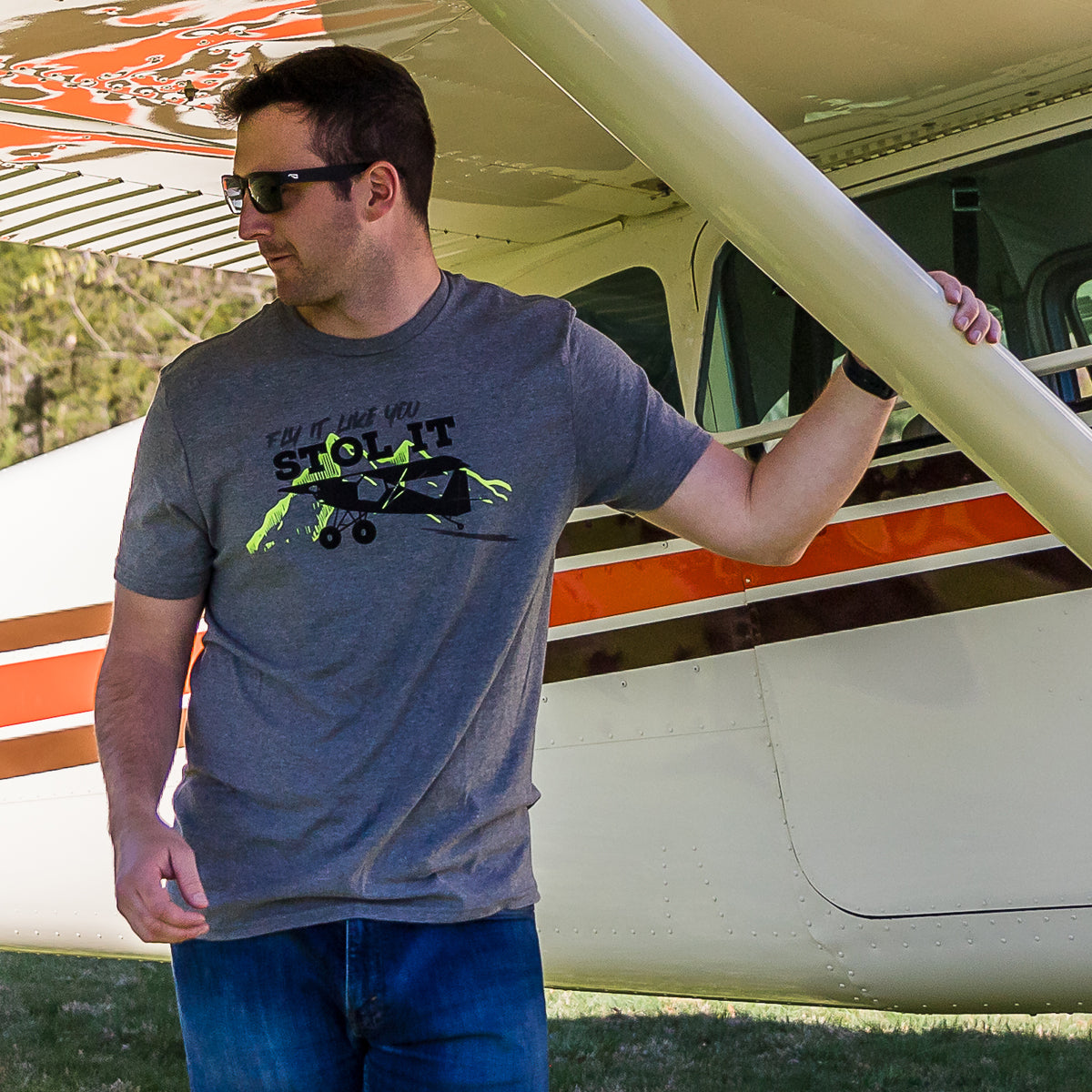 Man wearing Flight Outfitters 'Fly It Like You STOL It' T-Shirt standing under aircraft wing